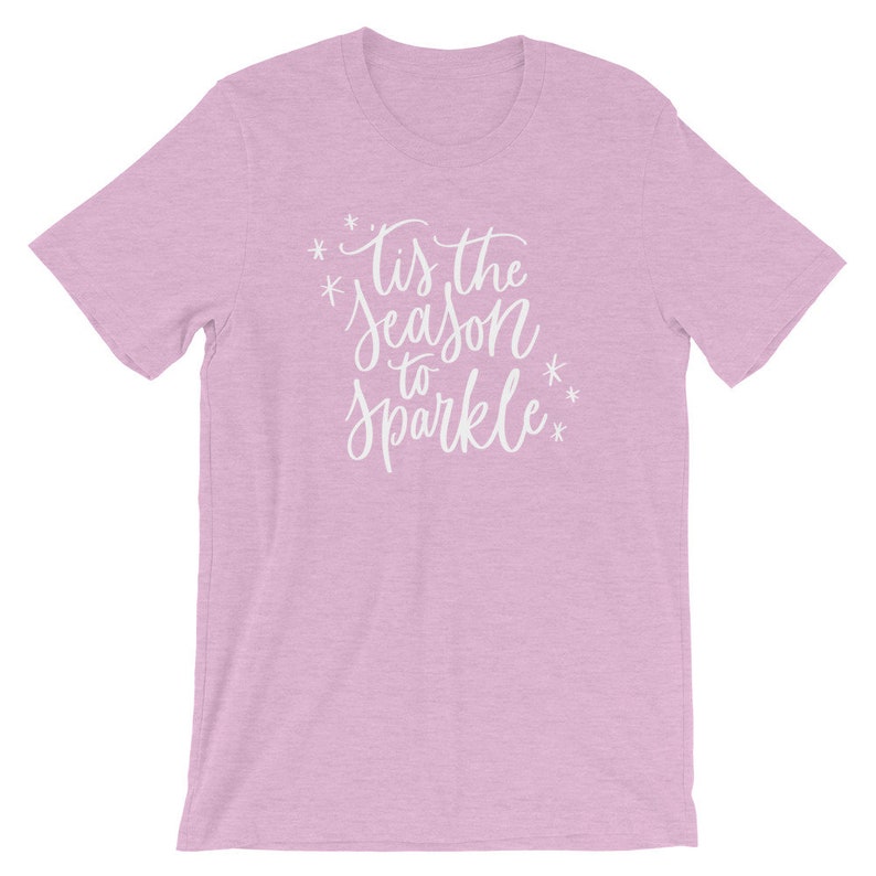May include: A light pink t-shirt with the text "Tis the season to sparkle" in white lettering.
