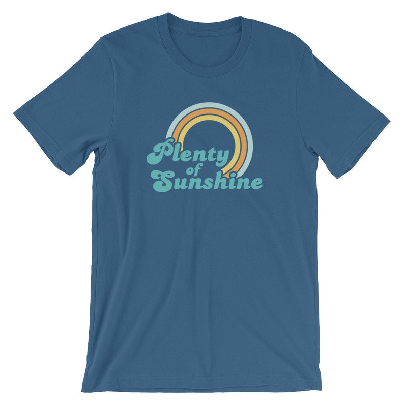 May include: A blue t-shirt with a retro design. The design features a rainbow with orange, yellow, and light blue arches, and the words "Plenty of Sunshine" in a retro font.
