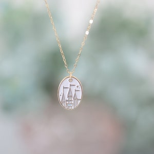 May include: A gold chain necklace with a white oval pendant featuring a gold outline of a castle with flags.