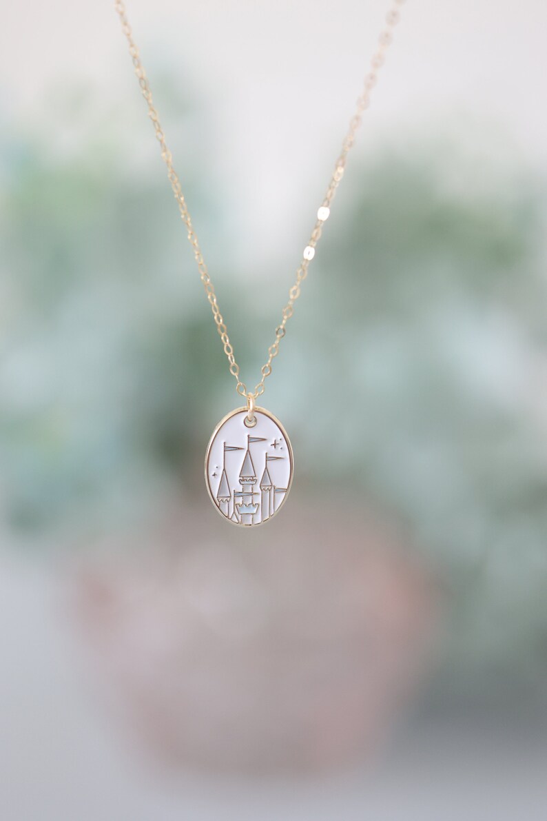 May include: A gold chain necklace with a white oval pendant featuring a gold outline of a castle with flags.