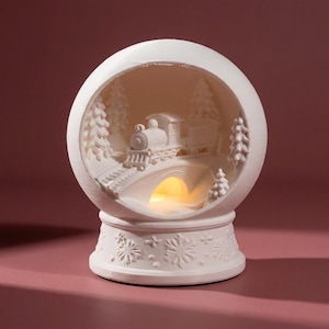 Könnte beinhalten: Ein weißes, kugelförmiges Keramikornament mit einem Relief einer Dampflokomotive, die eine Brücke überquert, umgeben von Tannenbäumen. Der Sockel ist mit Schneeflockenmustern verziert und das Innere strahlt ein warmes gelbes Licht aus.