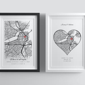 Puede incluir: Dos impresiones enmarcadas de mapas de ciudades en blanco y negro con puntos rojos. Una es rectangular, la otra en forma de corazón. El texto incluye nombres, fechas y la frase "Where it all began."
