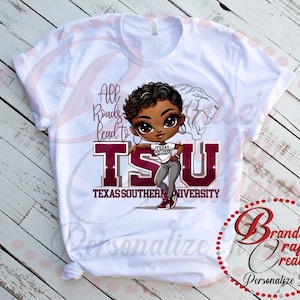 Könnte beinhalten: Weißes T-Shirt mit einer Cartoon-Illustration eines schwarzen Mädchens, das ein rotbraunes und graues "TSU"-Shirt und Jeans trägt. Der Text "All Roads Lead to TSU" und "Texas Southern University" ist auf dem Shirt aufgedruckt.