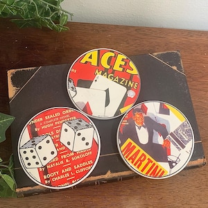 May include: Three vintage round coasters with retro designs. One coaster features the text "ACES MAGAZINE" with playing cards. Another shows dice and the text "UNDER SEALED ORD". The third coaster has a man in a tuxedo and the word "MARTINI".