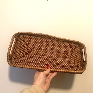 May include: A rectangular woven rattan tray with integrated handles. The tray is a warm brown color and features a tightly woven pattern. The handles are sturdy and seamlessly integrated into the design. This tray is suitable for serving or decorative purposes.