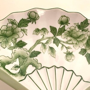 Op de afbeelding: Witte, waaiervormige decoratieve schaal met een groen bloemmotief. Het ontwerp toont groene pioenrozen, knoppen en bladeren op een tak. De schaal heeft een geschulpte rand en een waaiervormig patroon.