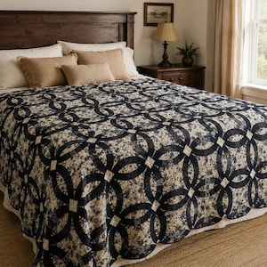 May include: A bed quilt featuring a dark navy blue and cream double wedding ring pattern. The fabric displays a dense floral print within the interlocking rings, accented by small cream-colored squares at the intersections of the circular design.