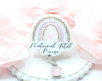 May include: A white badge reel with a pink, blue, and brown leopard print rainbow design. The text "Maternal Fetal Nurse" is written on the badge reel. A pink glitter charm is attached to the reel.