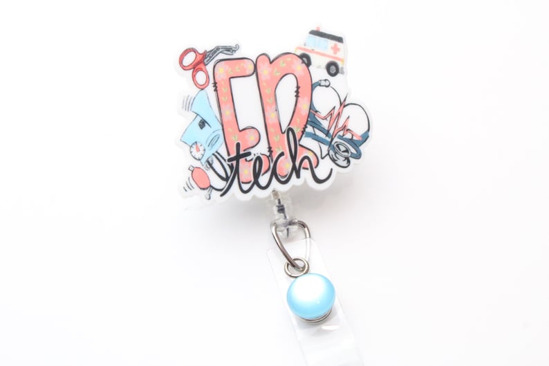 May include: A white and pink retractable badge holder with a blue button. The holder features a cartoon illustration of medical equipment and the text "ER tech".