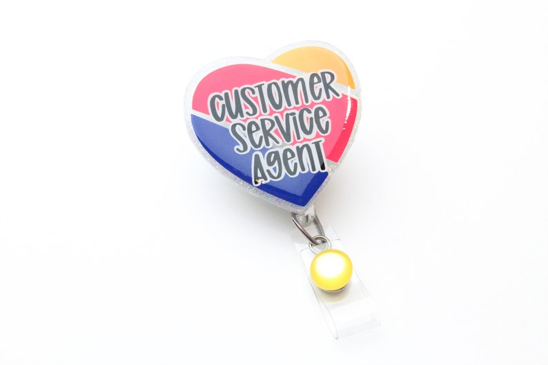 May include: A heart-shaped badge holder with a red, blue, and yellow design. The badge holder has the text "Customer Service Agent" printed on it.
