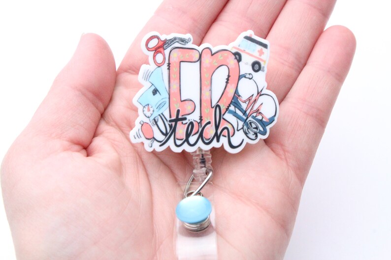 May include: A white and pink badge reel with the text "ER Tech" and medical illustrations. The reel has a blue button and a clear plastic cord.
