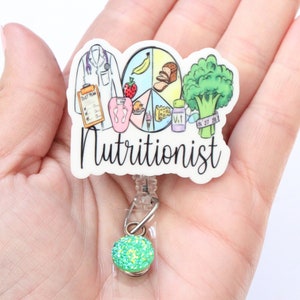 May include: White badge reel with a colorful illustration of a doctor, food groups, and the word "Nutritionist". The badge reel has a green glitter charm.