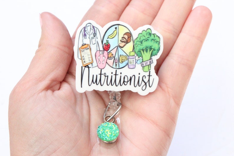 May include: White badge reel with a colorful illustration of a doctor, food groups, and the word "Nutritionist". The badge reel has a green glitter charm.
