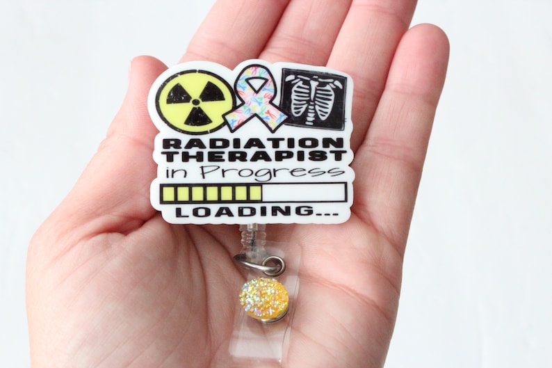 May include: White badge holder with a radiation symbol, a pink ribbon, and an x-ray image of lungs. The text reads "Radiation Therapist in Progress" with a yellow progress bar and the words "LOADING..." below.