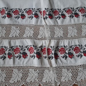 May include: A white textile featuring horizontal bands of intricate floral embroidery in red and black thread, alternating with wide sections of openwork crochet lace. The fabric displays a repeating pattern of roses and leaves throughout the design.