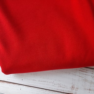 Peut inclure: Un tissu rouge vif, possiblement un textile ou un matériau, est présenté. Le tissu est plié, révélant sa texture et sa couleur. Le fond est une surface en bois blanc, contrastant avec le rouge vif.