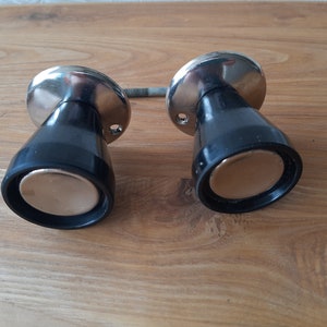 May include: Two vintage door knobs with a black conical base and a shiny silver top. The knobs have a circular, gold-colored center. A threaded rod connects the two knobs, suggesting they are a set.