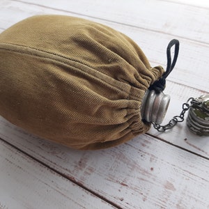May include: An olive-drab canvas canteen with a matching cover and a metal cap. The canteen has a black drawstring closure and a chain connecting the cap. The cap is painted green and has a worn appearance. The canteen is designed for carrying water.