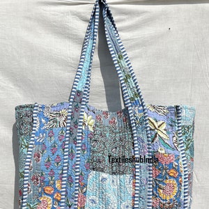 May include: A large blue and white patchwork tote bag with floral patterns. The bag has long straps and is made of quilted fabric. The text "Textileshubindia" is visible on the bag.