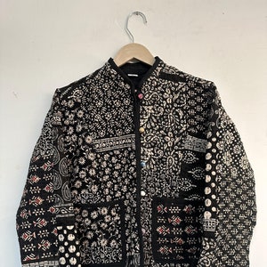 May include: A black quilted jacket with a white and black patterned design. The jacket has a mandarin collar, a button closure, and two patch pockets.