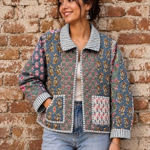 May include: A quilted jacket featuring a patchwork of blue, green, and pink floral and paisley patterns. The garment has a fold-over collar, long sleeves with striped cuffs, and two front patch pockets, all finished with black and white striped trim.