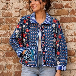 Puede incluir: Una chaqueta acolchada con base azul y un estampado floral multicolor en rojo y blanco. La chaqueta tiene un cuello vuelto, mangas largas con puños a rayas y dos bolsillos delanteros de parche. Los bordes están adornados con rayas azules y blancas.