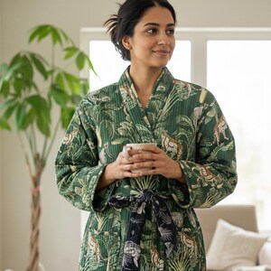 May include: A green quilted robe with a jungle-themed pattern featuring leopards and foliage. The robe has a black and white patterned tie and is worn by a person holding a white mug. The robe is made of a soft, comfortable material.