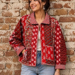 May include: A quilted jacket featuring a patchwork of red floral and botanical patterns, a fold-over collar with white and red stripes, long sleeves with striped cuffs, two front patch pockets, and a button-down front closure with white stitching.