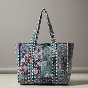May include: A patchwork tote bag with a floral design in blue, pink, and green. The bag has striped handles in white and green. The bag is a medium size, suitable for everyday use. The bag is made of quilted fabric.