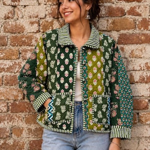 May include: A quilted jacket featuring a patchwork design in shades of dark green and olive, adorned with floral and botanical patterns. The jacket includes a collared neckline, long sleeves with striped cuffs, and two front patch pockets with blue accents.