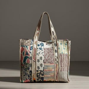 May include: A patchwork tote bag with a rectangular shape and two handles. The bag features a variety of fabric patterns in shades of blue, red, and cream. The edges are trimmed with a cream-colored fabric.