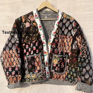 以下が含まれることがあります： 花柄のパッチワークデザインの黒いキルティングジャケット。ジャケットはVネック、長袖、ボタン留め。生地は花柄、幾何学模様、ペイズリーなど、さまざまなプリントとパターンがミックスされています。