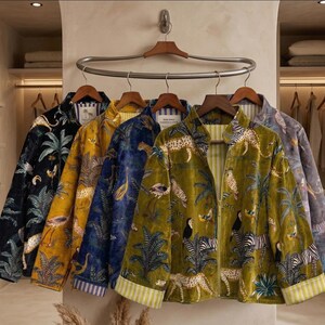 May include: Five velvet jackets with animal and plant prints, in black, yellow, blue, olive green, and grey. Each jacket features a different design, including leopards, zebras, and birds. The jackets are displayed on wooden hangers, showcasing their unique patterns.
