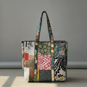 Puede incluir: Un bolso tote patchwork con una variedad de patrones y colores de tela. El bolso presenta una mezcla de diseños florales, geométricos y abstractos en tonos de verde, rosa, azul y negro. Las asas y el ribete tienen un patrón de cuadros blancos y negros.