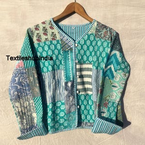 May include: A teal blue quilted jacket with a patchwork design. The jacket has a button closure and long sleeves. The fabric is made of cotton and has a variety of patterns, including floral, geometric, and striped. The text "TextileshubIndia" is visible on the jacket.