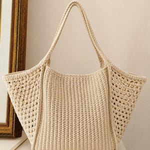 Può includere: Una borsa tote all'uncinetto fatta a mano color crema. La borsa presenta una base rettangolare e una parte superiore ampia e aperta con due manici robusti. I lati hanno un design traforato unico, mentre il centro presenta un motivo a punto verticale pieno.