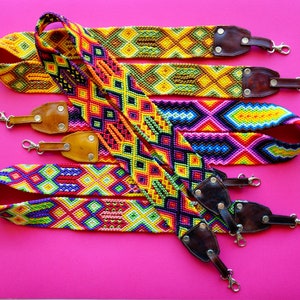 May include: Four colorful woven camera straps with leather accents and metal clasps. The straps feature geometric patterns in shades of yellow, red, blue, green, and purple.