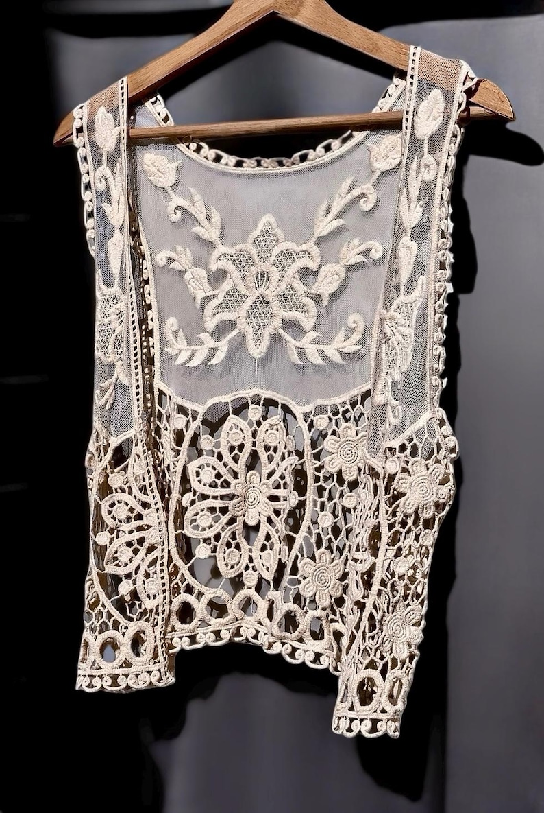 May include: A cream-colored crochet vest with a floral design. The vest is sleeveless and has a delicate, openwork pattern.