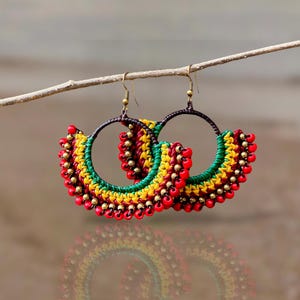 May include: A pair of hoop earrings made with red, yellow and green beads. The earrings are hanging from a twig.
