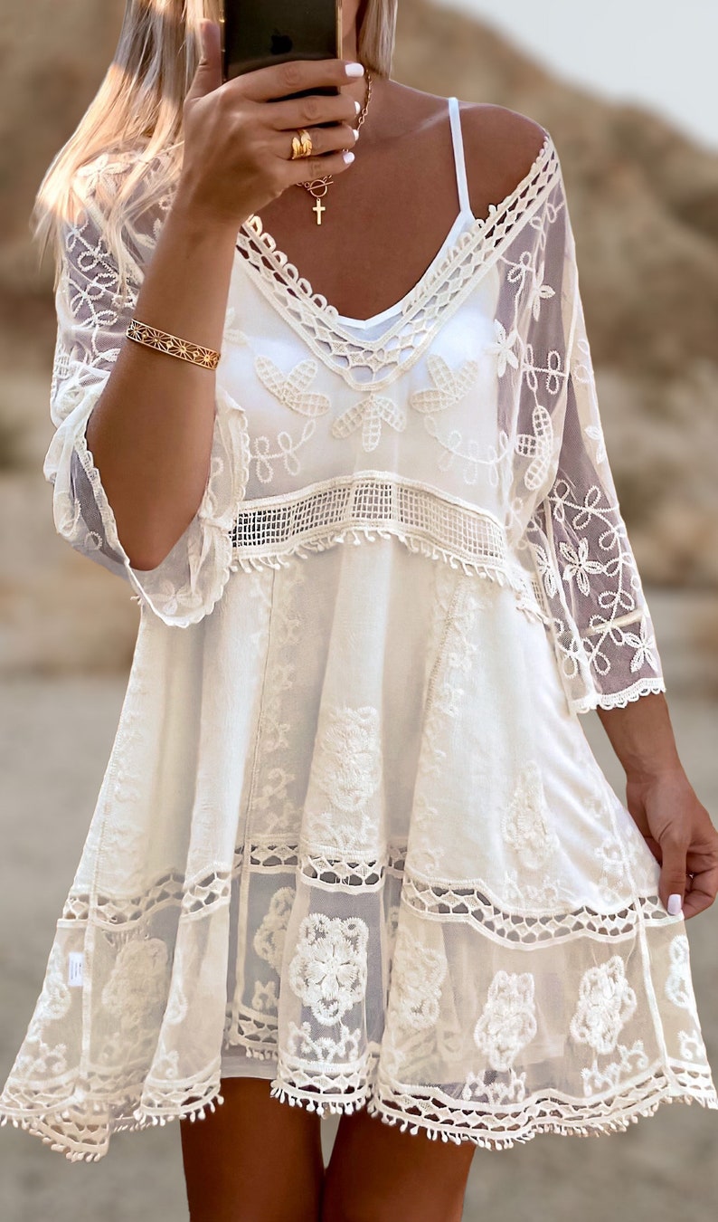 May include: White crochet dress with a lace overlay and a scalloped hem. The dress has a V-neckline and 3/4 sleeves.