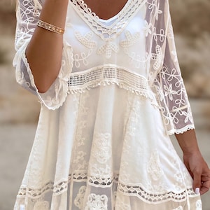 May include: White crochet dress with a lace overlay and a scalloped hem. The dress has a V-neckline and 3/4 sleeves.