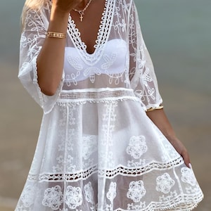 May include: White crochet beach cover-up with a V-neckline and delicate floral embroidery. The cover-up has a loose fit and a flowy silhouette.