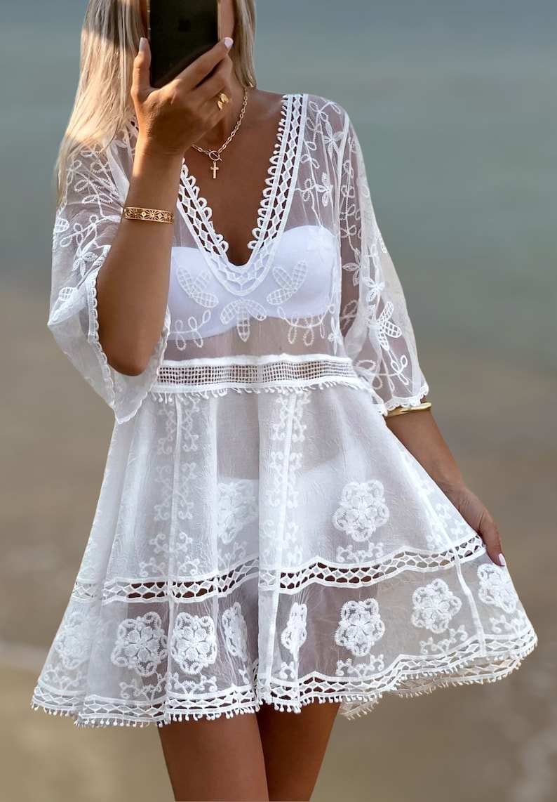 May include: White crochet beach cover-up with a V-neckline and delicate floral embroidery. The cover-up has a loose fit and a flowy silhouette.