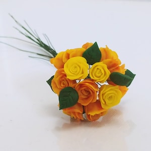May include: A bouquet of small, yellow and orange roses with green leaves. The roses are arranged in a circular shape and have a delicate, romantic look.