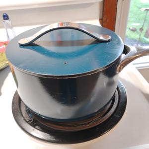 Op de afbeelding: Een diepblauwe steelpan met een bijpassend deksel en een zilverkleurige metalen handgreep. De pan heeft een gladde, glanzende afwerking en een kleine stoomopening in het deksel. De handgreep is stevig aan de zijkant van de pan bevestigd.