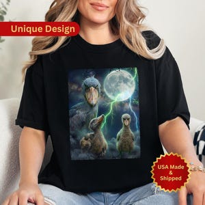 May include: Black t-shirt featuring a unique design with a Shoebill stork family under a full moon with lightning. The text "Unique Design" is at the top left. The text "USA Made & Shipped" is at the bottom right.