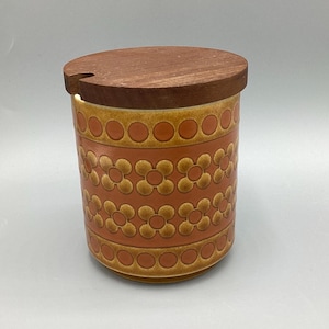 May include: A ceramic jar with a wooden lid. The jar is cylindrical with a floral pattern in shades of orange and brown. The lid has a small notch. The jar is likely for kitchen storage.