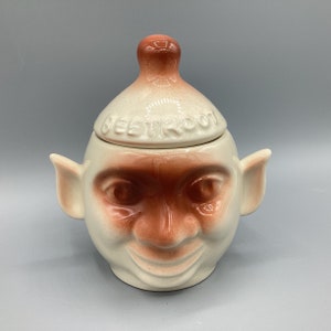 May include: A white ceramic sugar bowl with a brown glaze and a whimsical face. The lid is also ceramic and has the words "Sweet Tooth" written on it.