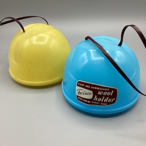 May include: Two vintage plastic wool holders in yellow and blue. The blue holder has a label that reads "Twinco wool holder". Each holder has a brown handle. The holders are light and unbreakable.
