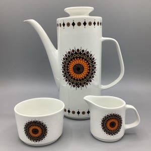 May include: A white ceramic coffee set comprising a coffee pot, creamer, and sugar bowl. Each item is adorned with a large orange and brown floral pattern and geometric detailing.